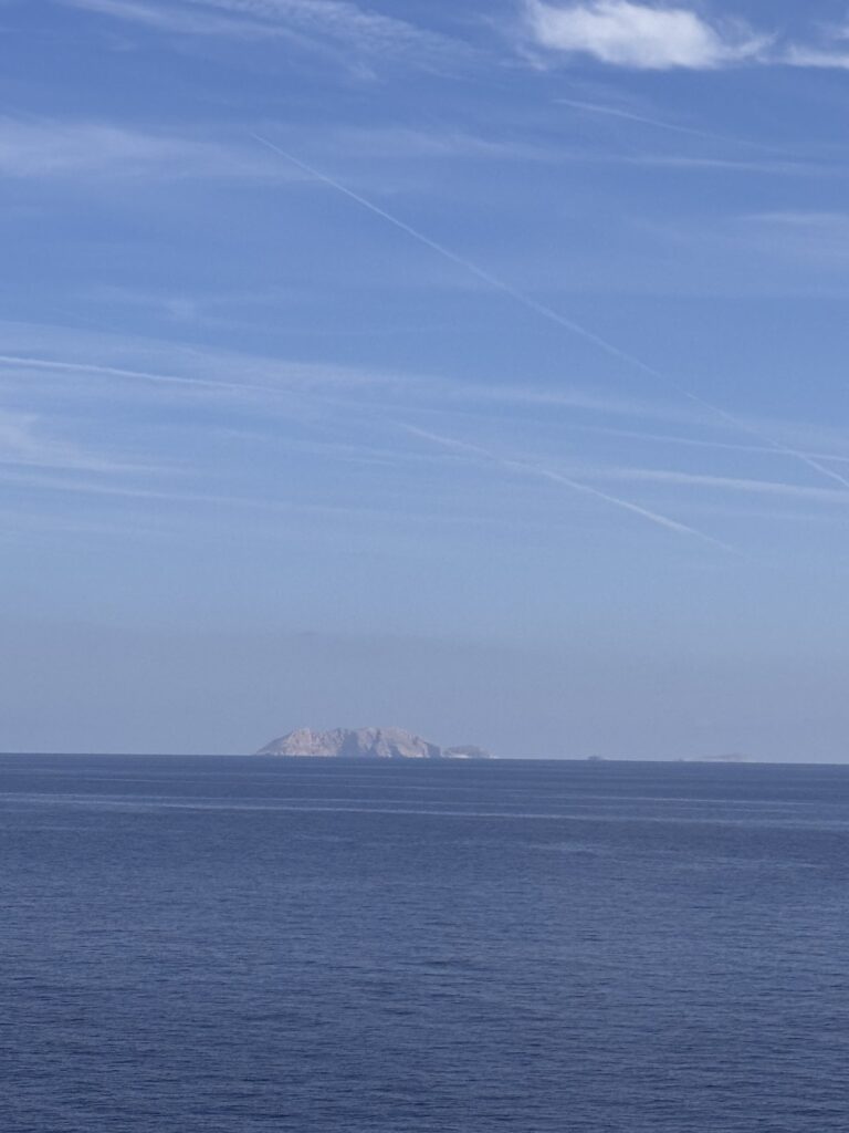 A rocky island on the horizon under a clear blue sky