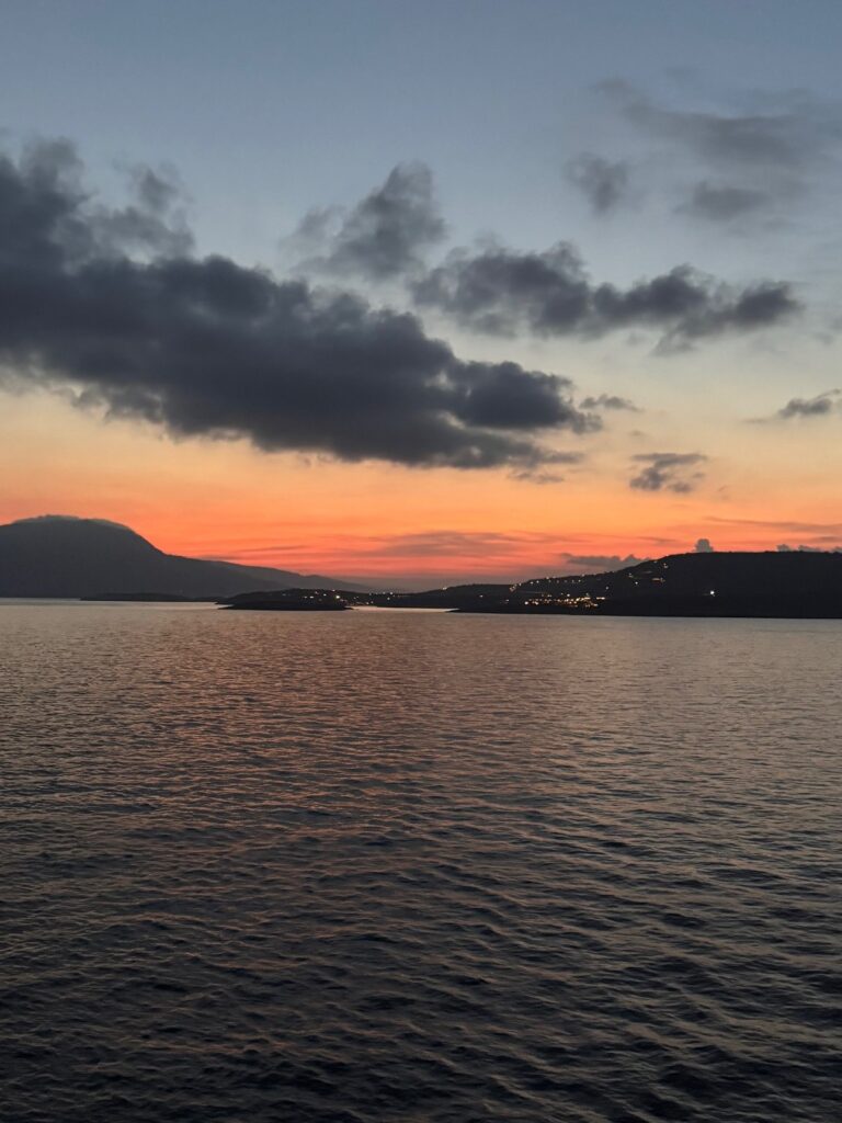 An orange sunset over a coastline and dark water
