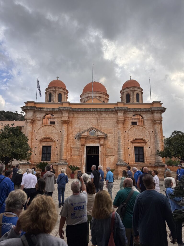 Pilgrims gathered before the orange stone church of the Agia Triada monastery