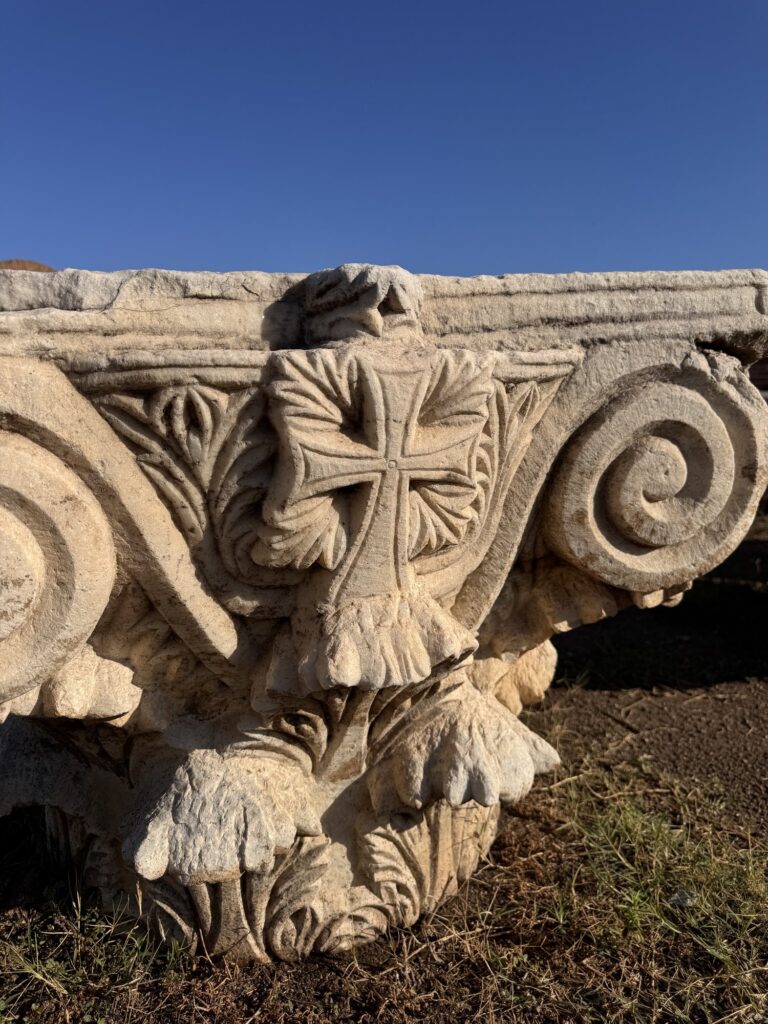 A carved marble capital with a cross among the ruins of the basilica