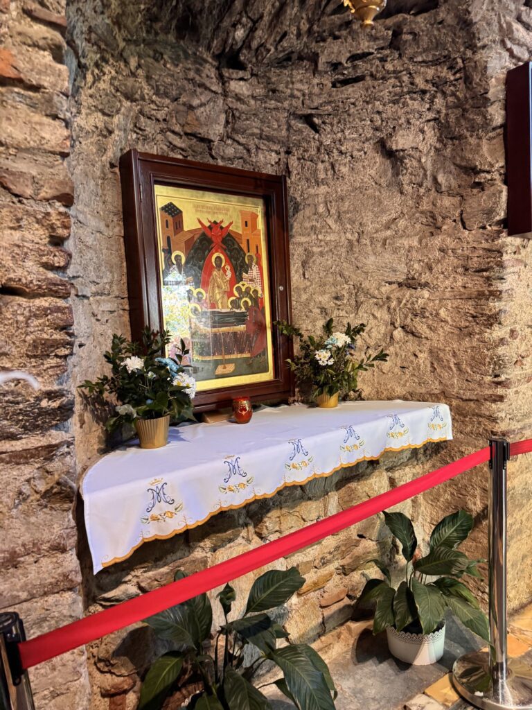 An icon above a white-draped altar with flowers inside the House of Mary