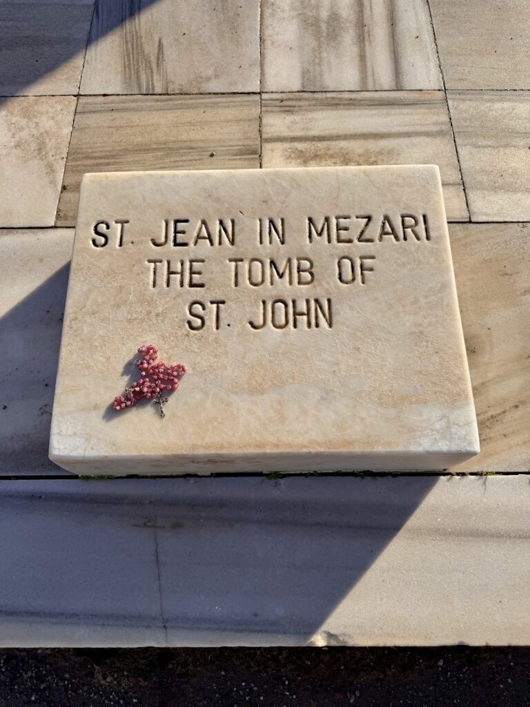 A marble slab inscribed St. Jean in Mezari, The Tomb of St. John, with a rosary laid on it