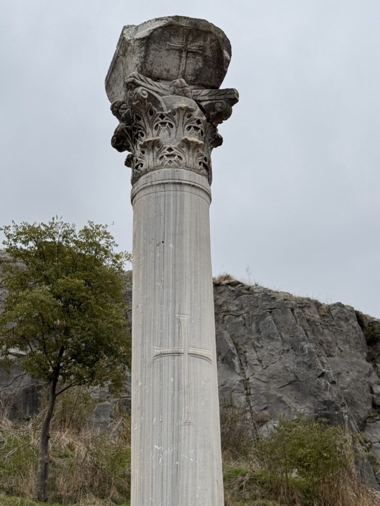 A tall marble column with a Corinthian capital and a carved cross, among the ruins of Philippi