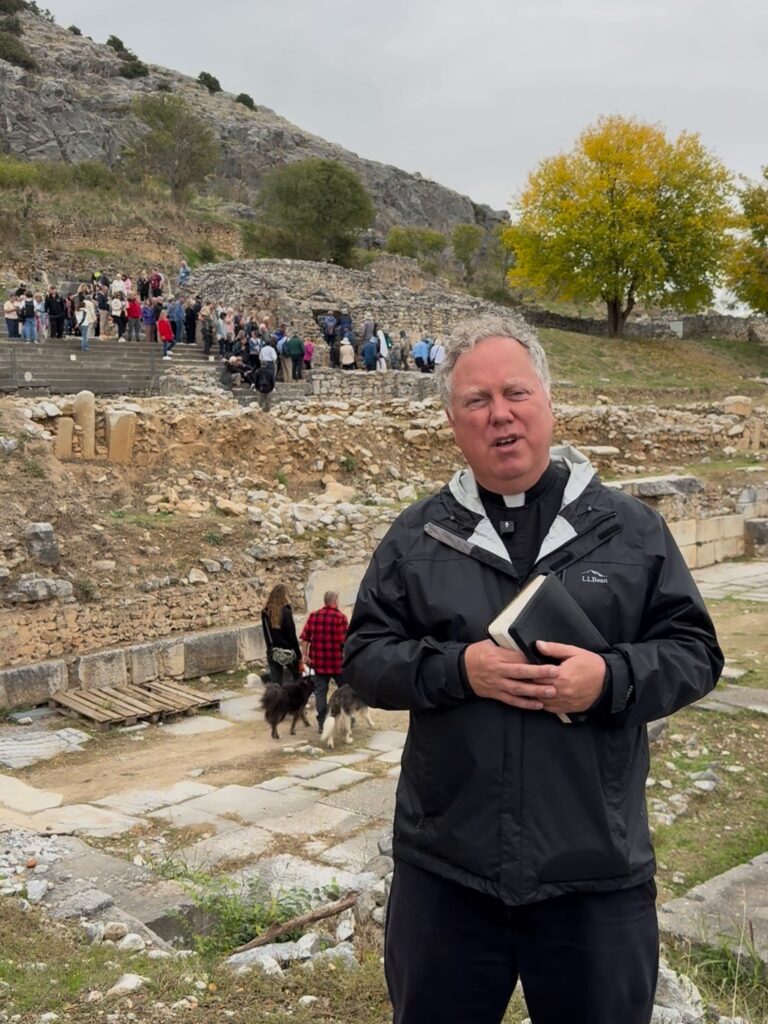 Fr. Jonathan Wilson speaking among the ruins of ancient Philippi, with pilgrims on the hillside behind him