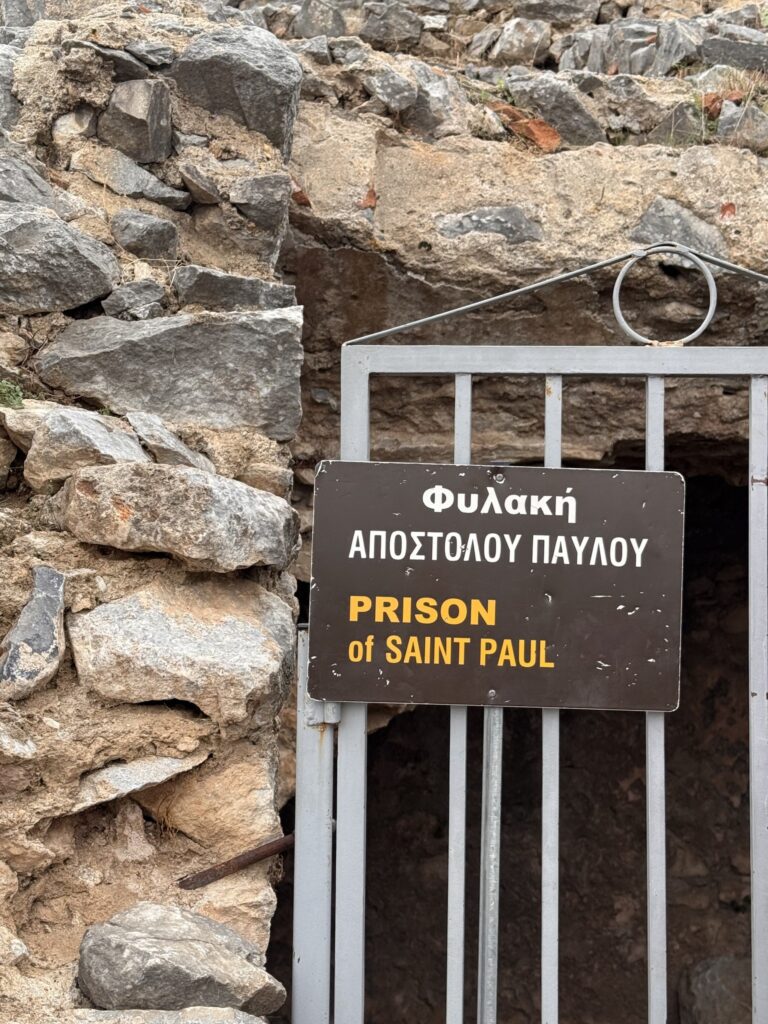A sign reading Prison of Saint Paul in Greek and English on a gate in an ancient stone wall