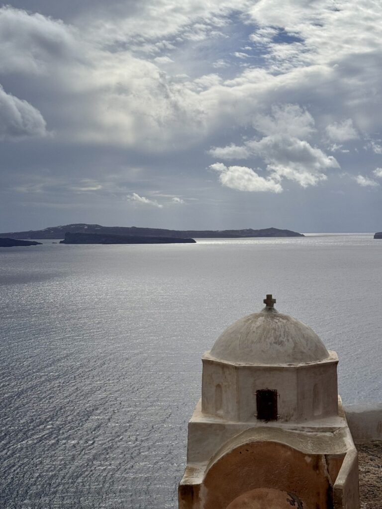 A small whitewashed chapel dome above the sea under a cloudy sky