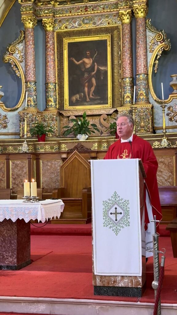 Fr. Jonathan Wilson in red vestments preaching at the ambo of the Catholic cathedral on Santorini