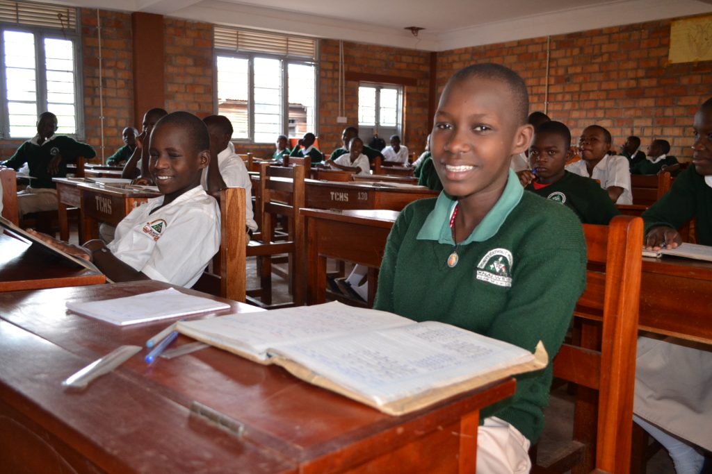 students in green uniforms sitting at desks in classroom