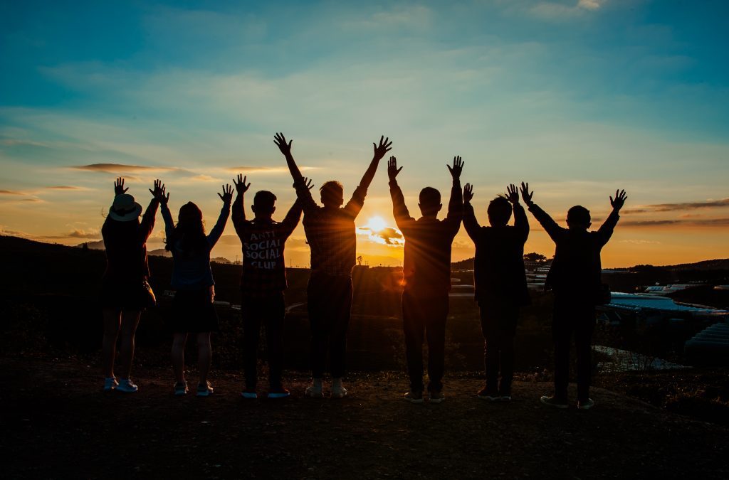silhouette of people jumping at sunset with hands raised